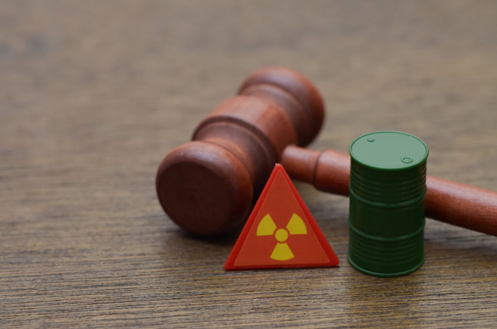 the legal ramifications of handling hazardous materials, featuring a judge's gavel, a miniature barrel, and a radiation warning symbol.