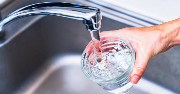 A faucet pouring water into a handheld glass.